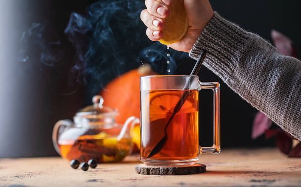 A womans hand squeezes lemon juice into a mug of tea. Autumn cozy composition. - Fotoğraf, Görsel