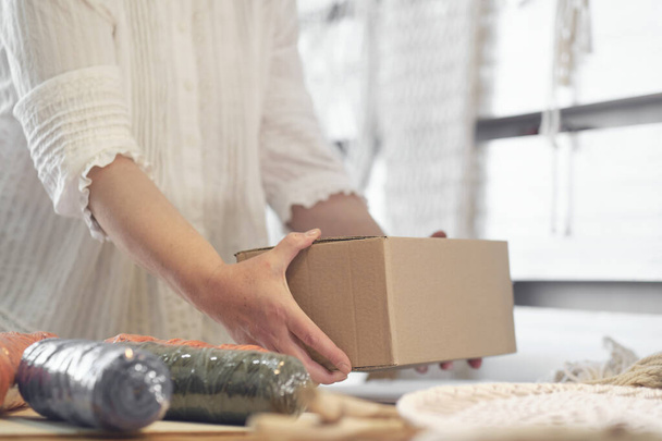 女性起業家は手作りの製品を段ボール箱に詰めます。小さなビジネスのための商品の配達。老人は家から趣味を得て. - 写真・画像