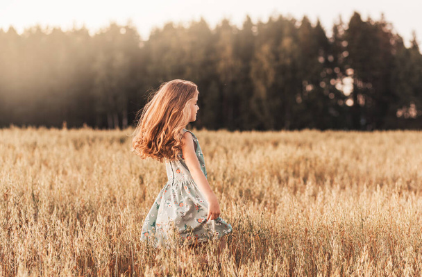 Mutlu küçük bir kız yazın güneşli bir günde buğday tarlasında koşar. Yaz zamanı. Yaz tatili. Mutlu bir çocukluk. Pozitif duygular ve enerji - Fotoğraf, Görsel
