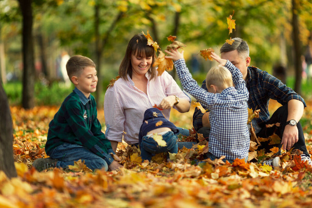 Family with children in the autumn park play with bright orange leaves. Happiness, love and good family relationships. Selective focus. - Foto, Bild