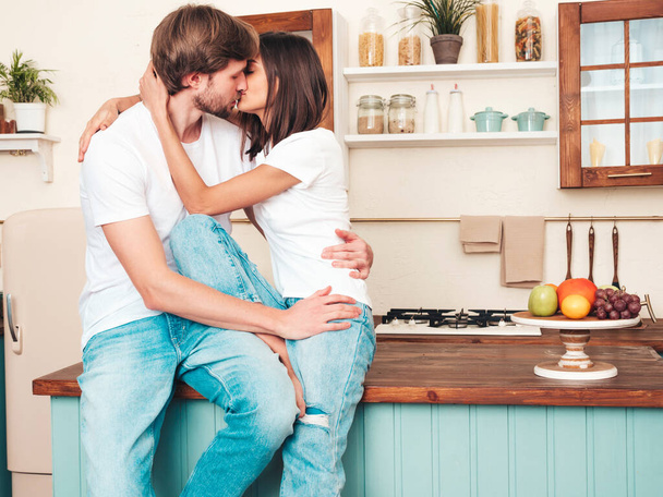 Smiling beautiful woman and her handsome boyfriend.Happy cheerful loving family having tender moments.Pure models making breakfast.Embracing each other.Cooking together in light kitchen. Kissing - Фото, зображення