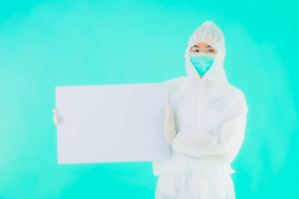 Portrait beautiful young asian doctor woman wear ppe or  personal protective equipment for protect from coronavirus or covid19 with empty card white board on blue isolated background - Photo, Image
