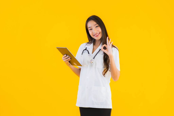 Porträt schöne junge asiatische Ärztin verwenden Smart-Tablet-Gerät auf gelbem Hintergrund isoliert - Foto, Bild