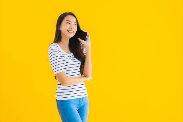 Портрет красива молода азіатська жінка посміхається щасливо використовувати смартфон на жовтому ізольованому фоні
 - Фото, зображення