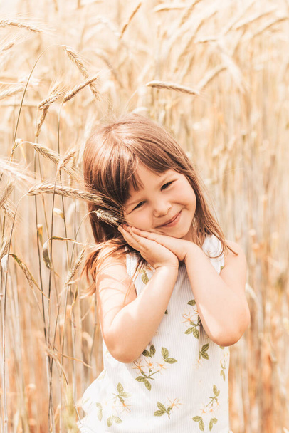 A little girl plays with spikelets in a wheat field - Фото, зображення