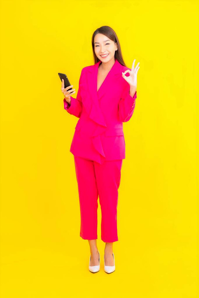 Portré gyönyörű fiatal ázsiai nő használ okos mobiltelefon sárga színű elszigetelt háttér - Fotó, kép