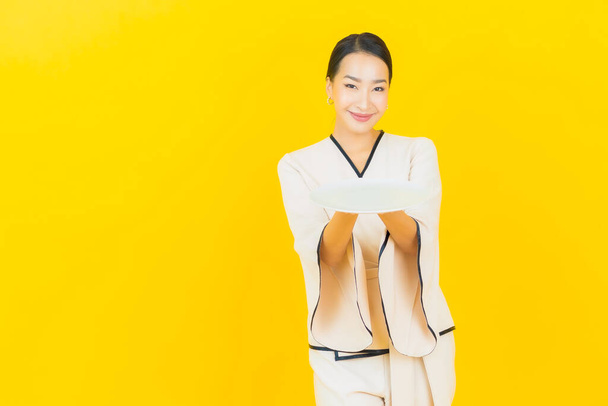 Retrato hermosa joven negocio asiático mujer con plato vacío plato sobre fondo amarillo - Foto, imagen