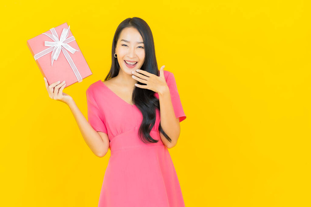 Portré gyönyörű fiatal ázsiai nő mosoly piros ajándék doboz sárga színű háttér - Fotó, kép