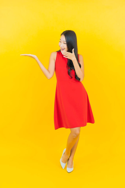 Güzel bir portre genç Asyalı kadın kırmızı elbiseler giyip sarı arka planda hareketli bir gülümseme takın. - Fotoğraf, Görsel