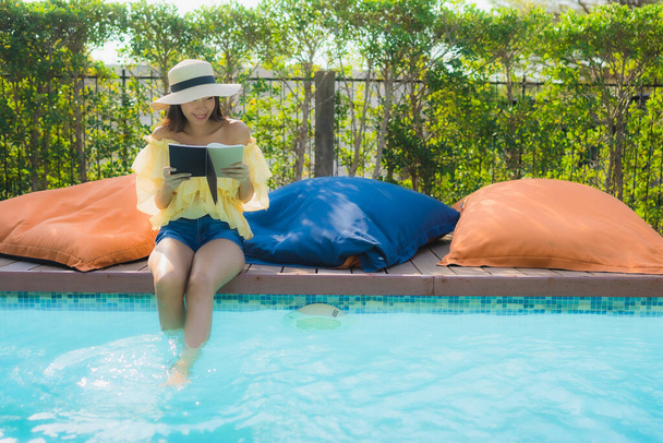 ポートレート若いアジアの女性はホテルリゾートの屋外スイミングプールの周りの本を読む - 写真・画像