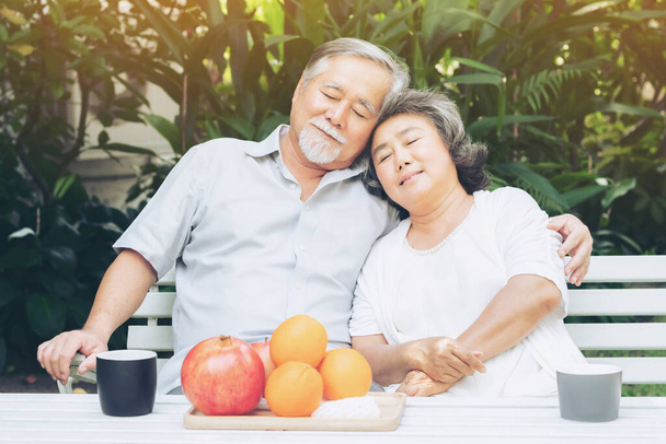 Anziani pensionati coppia si siedono abbracciando l'un l'altro e rilassarsi per l'ora del caffè mattina nel cortile con felicità e sorrisi - stile di vita anziano coppia amore concetto sano - Foto, immagini