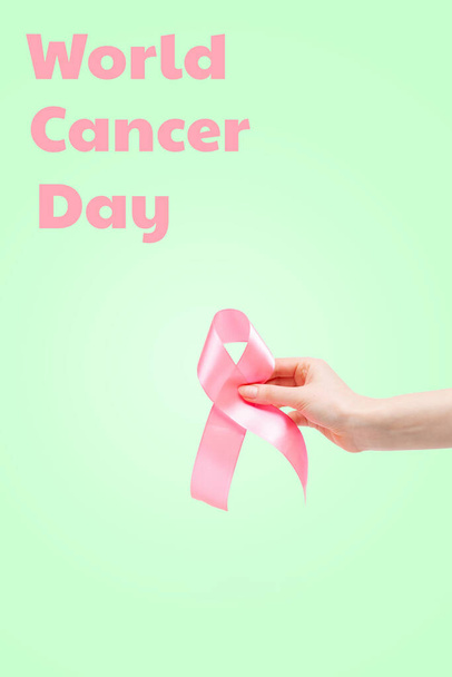 世界癌の日。薄緑色の背景にピンクのリボンをつけた女性の手。垂直方向。スペースのコピー. - 写真・画像