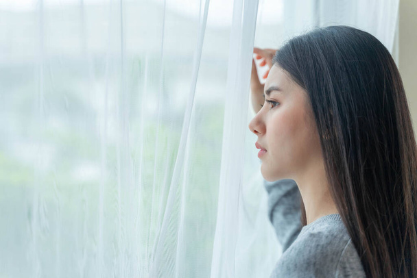 Een jonge vrouw die met angstige ogen uit het raam van haar huis kijkt. Alsof je wacht tot iemand terugkomt. - Foto, afbeelding