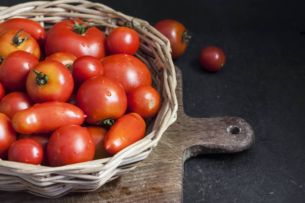 Verse rode tomaten in wittere mand op zwarte achtergrond. - Foto, afbeelding