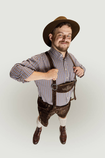 Portrét šťastného vousatého muže, číšníka v tradičním rakouském nebo bavorském kostýmu, stojícího sám nad šedým pozadím. Funny meme emotions - Fotografie, Obrázek