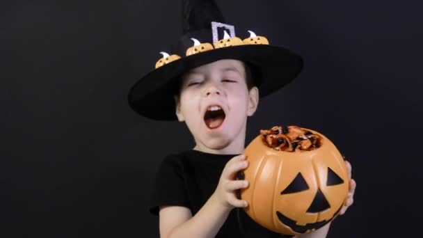 Un niño de Halloween sostiene una calabaza con dulces y gritos, canta canciones. Preparación para las vacaciones - Imágenes, Vídeo