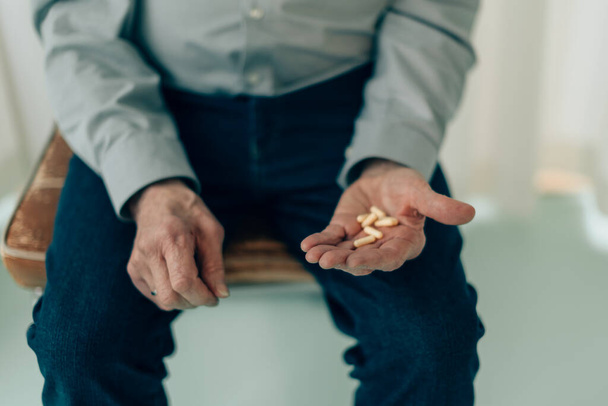középső részén idős férfi ül széken tartja gyógyszer tabletták tenyérbe - fucus ujjakon - Fotó, kép