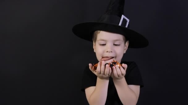 Dzieciak Halloween. Chłopiec w stroju czarownicy trzyma cukierka na czarnym, liże usta, cukierek spada - Materiał filmowy, wideo