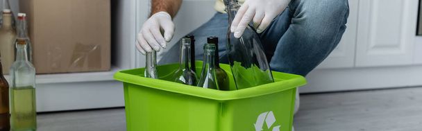 Vista cortada do homem em luvas de látex segurando garrafa perto da caixa com sinal de reciclagem, banner  - Foto, Imagem