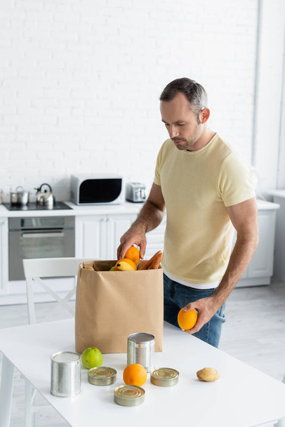 Man taking fruits from paper bag on table in kitchen  - Photo, Image