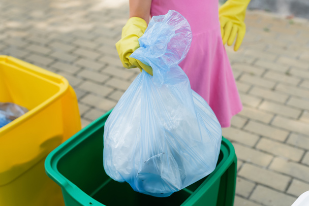 Καλλιεργημένη άποψη του κοριτσιού κρατώντας σακούλα σκουπιδιών κοντά σε κάδο σε εξωτερικούς χώρους  - Φωτογραφία, εικόνα