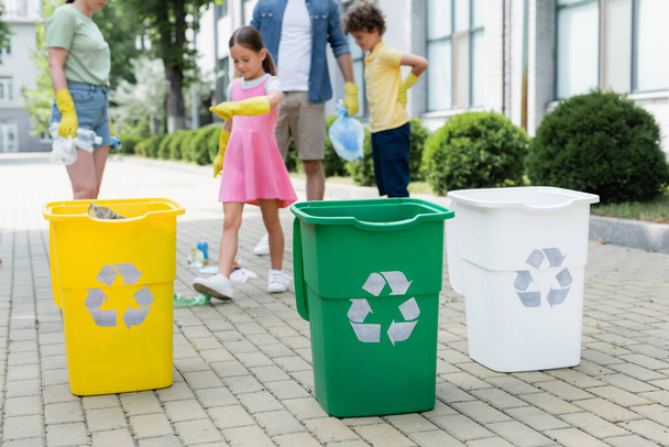Mülltonnen mit Recyclingschild nahe verschwommener Familie im Freien  - Foto, Bild