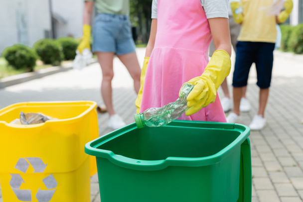 Cropped view of girl in rubber gloves holding bottle near trash can outdoors  - Foto, immagini