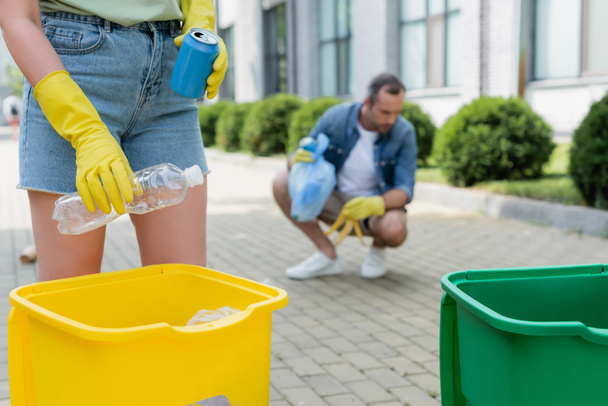 Cropped view of woman holding trash near can and blurred husband outdoors  - Photo, Image