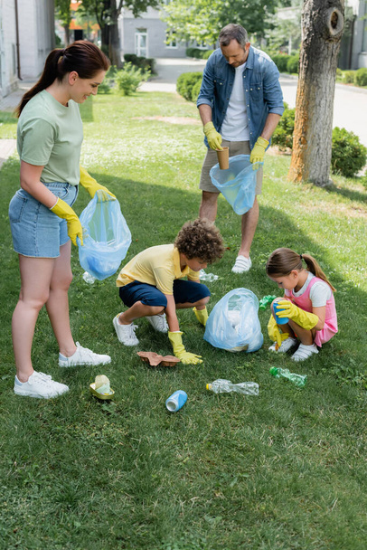 Family in rubber gloves collecting garbage on grass outdoors  - Φωτογραφία, εικόνα