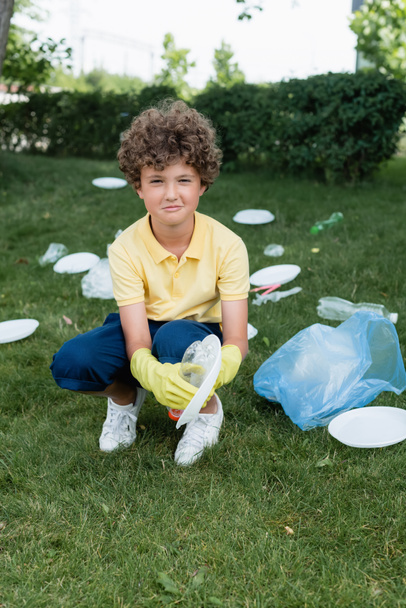 Glimlachend kind in rubberen handschoenen verzamelen van afval op het gazon  - Foto, afbeelding