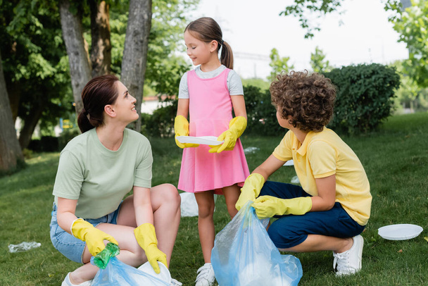 Smiling mother and kids collecting garbage on grass outdoors  - Foto, immagini