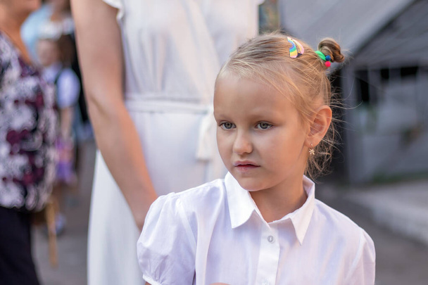 Porträt eines Kindes, Erstklässlerin, mit hübschem Gesicht, 7 Jahre alt, europäisch, blond, in weißer Bluse - Foto, Bild