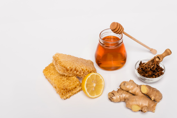 pot de miel près de trempette en bois, bol avec graines d'anis, nid d'abeille, citron frais et racine de gingembre sur blanc - Photo, image