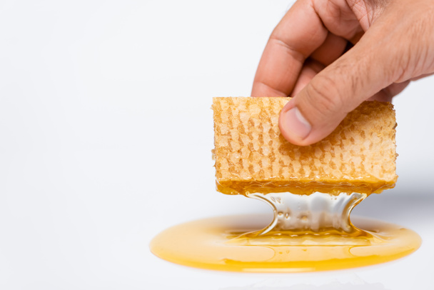 vista recortada del hombre sosteniendo panal con miel fresca y líquida en blanco - Foto, Imagen