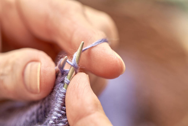 Woman is knitting a blue warm sweater. A hobby of elderly woman is knitting. Closeup view of knitting loop. Selective focus - Фото, изображение