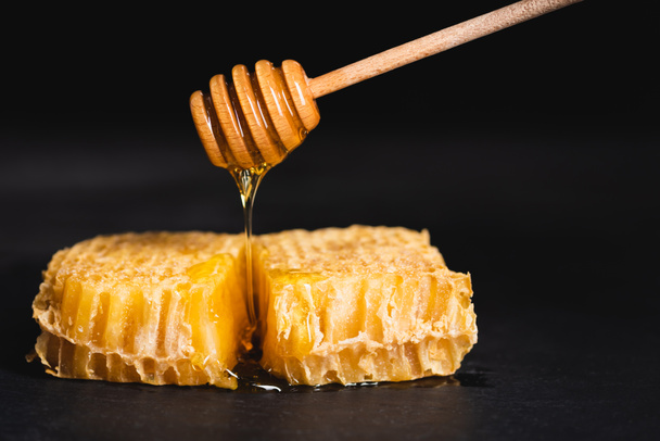 wooden dipper with liquid honey flowing on honeycomb isolated on black - Фото, зображення