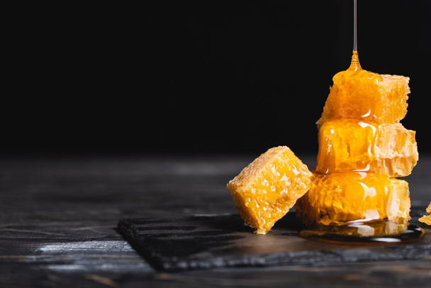 golden honey flowing on pieces of honeycomb on dark surface isolated on black - Foto, imagen