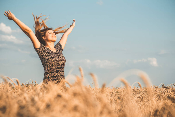 happy beautiful young woman enjoying nature, raising hands on background of cloudy sky in wheat field, girl breathe breathes deeply , freedom and relaxation concept - 写真・画像