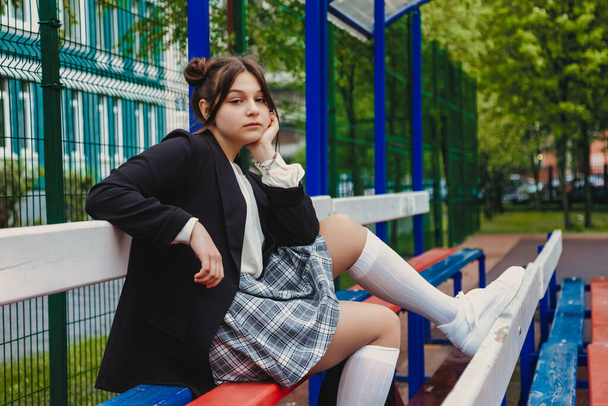 Art noise film style image. Portrait of thirteen-year-old schoolgirl in white blouse, plaid skirt and jacket at school. Emotional teen girl posing looking at camera. Concept of school age and learning - Foto, afbeelding