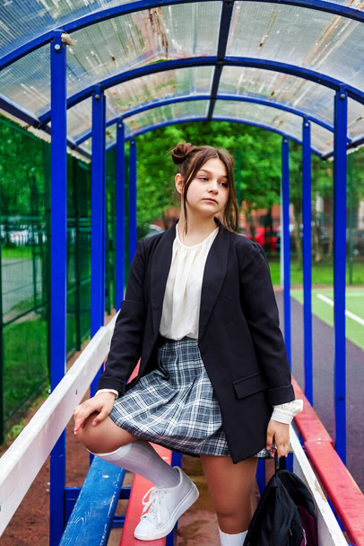 Art noise film style image. Portrait of thirteen-year-old schoolgirl in white blouse, plaid skirt and jacket at school. Emotional teen girl posing looking at camera. Concept of school age and learning - Фото, зображення