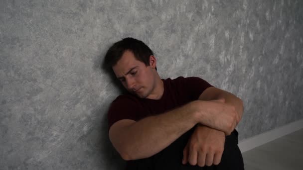 smutny i sfrustrowany mężczyzna siedzący przy ścianie - Materiał filmowy, wideo