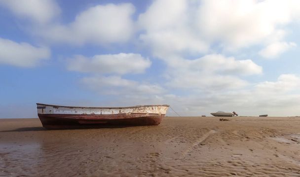 Um barco de pesca tradicional repousa em uma praia de areia. Pequena embarcação de remo de madeira fora de água na costa do rio com céu azul e fundo de nuvens. Um belo dia no custo do mar do sul da Espanha. - Foto, Imagem
