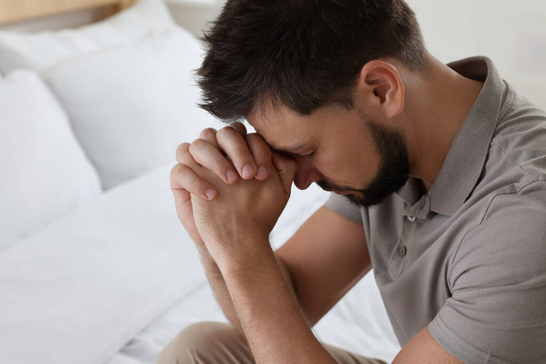 Religious man with clasped hands praying in bedroom - Photo, Image