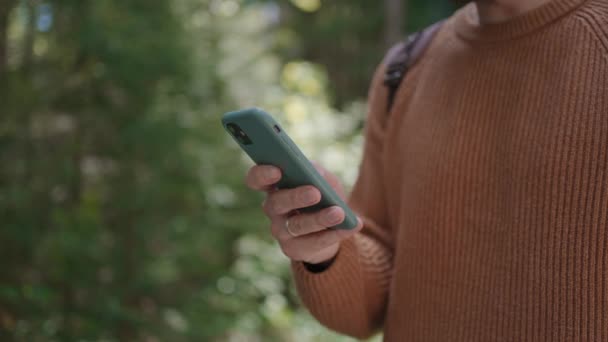 Een mobiele telefoon in handen van een jongeman die door het bos reist. Navigator, boodschapper en sociale netwerken. Gebruik uw mobiele telefoon om informatie te zoeken, voor een wandeling in het bosgebied. - Video