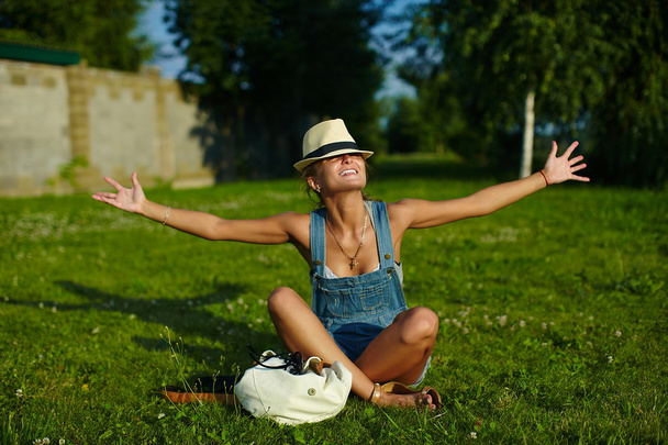 Portrait of cute funny young stylish smiling woman girl model in casual modern cloth with perfect sunbathed body outdoors in the park in hat - Fotó, kép