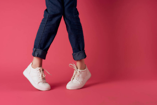 female legs in white sneakers in fashion posing pink background - Фото, изображение