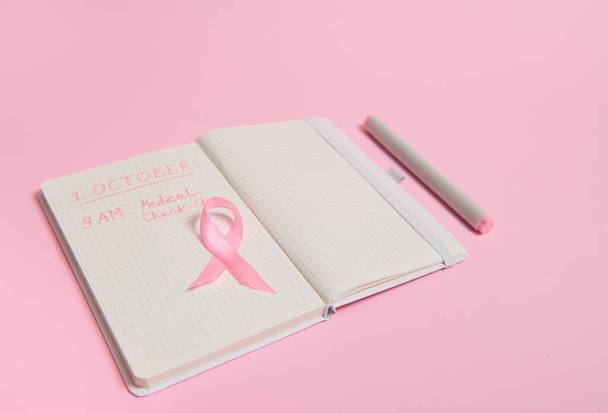 Korkea kulma näkymä vaaleanpunainen nauha, on avattu päiväkirja, jossa merkinnät muistuttaa lääkärintarkastus. 1. lokakuuta, Maailman rintasyöpäpäivä, Naisten terveydenhuolto ja lääketieteelliset käsitteet. - Valokuva, kuva