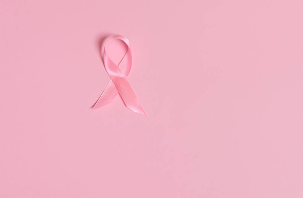 Flat lay of a satin pink ribbon awareness, International symbol of Breast Cancer Awareness Month in October. Isolated over on pink background with copy space . Women's health care and medical concept. - Foto, afbeelding