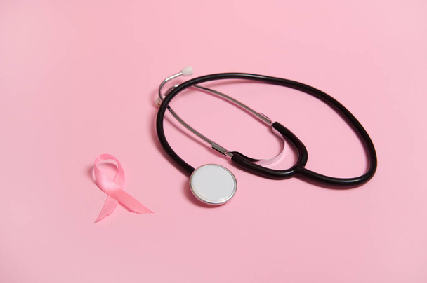 Sthetoscope and a satin pink ribbon awareness, International symbol of Breast Cancer Awareness Month in October. Isolated on pink background with copy space .Women's health care and medical concept. - 写真・画像