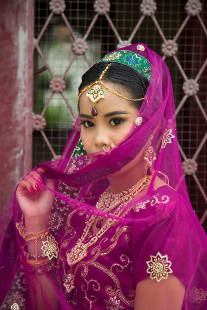 Portrait Asian woman in a margenta Indian tradition sari, she is looking at down at side a wrought iron door - Photo, Image